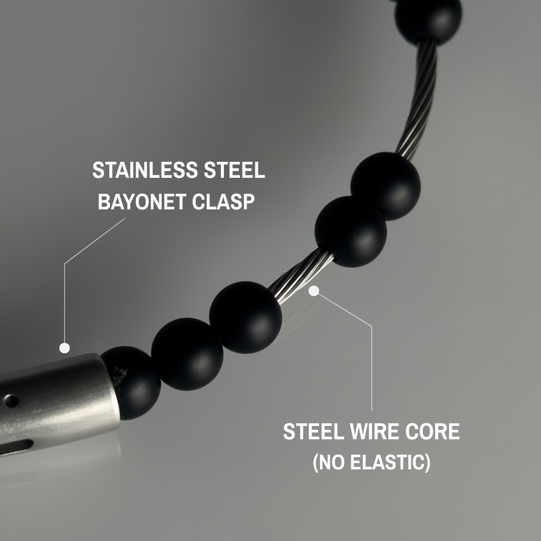 Close-up of a black beaded necklace with stainless steel clasp and steel wire core on a gray background.